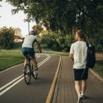 A cyclist and a walker enjoy a peaceful park trail surrounded by greenery.